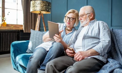 un couple de senior assis dans un canapé regardant une tablette numérique