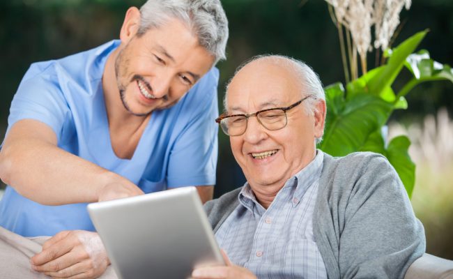 photo d'un soignant et d'un homme agé regardant une tablette numérique en souriant